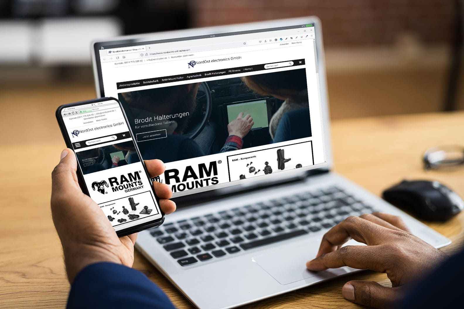 Eine Person hält ein Smartphone in der Hand, auf dem die NordOst-Website angezeigt wird, während sie einen Laptop benutzt, auf dem die gleiche Website geöffnet ist, auf der die Produkte von RAM Mounts vorgestellt werden.